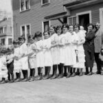 There are as many as thirteen children in this family, all lined up in a row. Now look at the car…