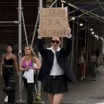 A woman is walking down the street with a large sign that says, “looking for a husband,” when something unexpected occurs.